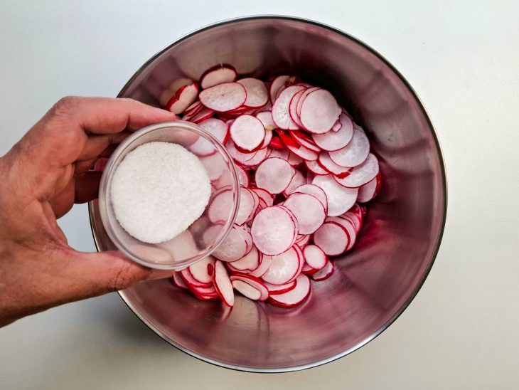 Sal sendo adicionado generosamente nas rodelas de rabanete.