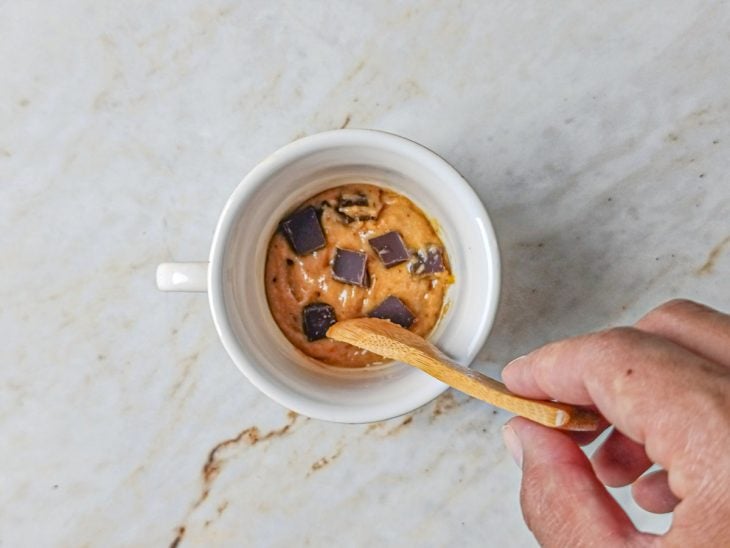 Pedaços de chocolate sendo misturados à massa na caneca.
