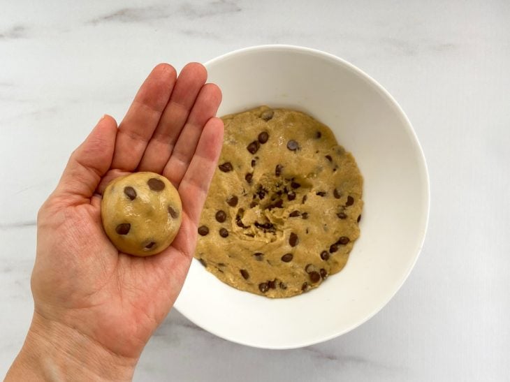 Uma mão segurando uma bolinha de massa de cookie cru.