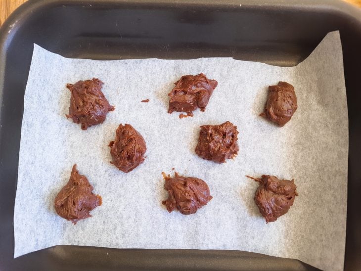 Porções de cookies acomodadas na assadeira forrada com papel manteiga.