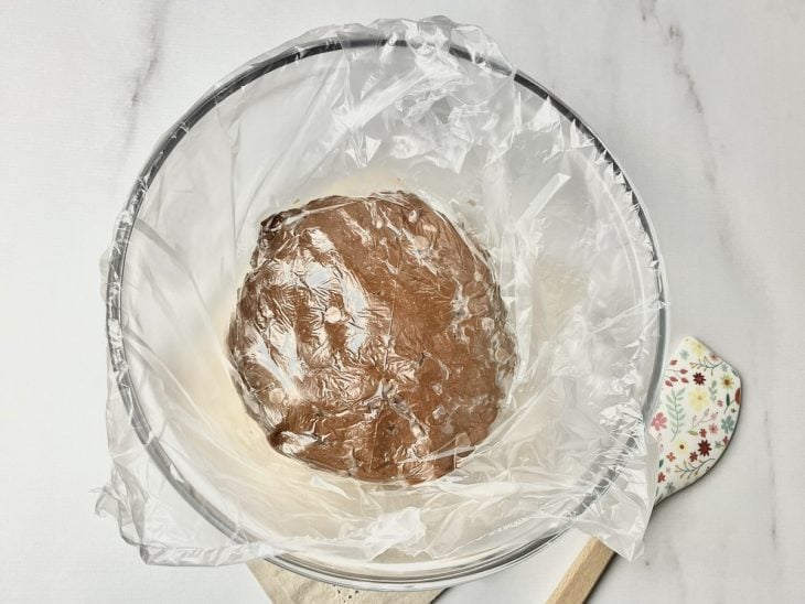 Recipiente com massa de cookie coberto por plástico filme.