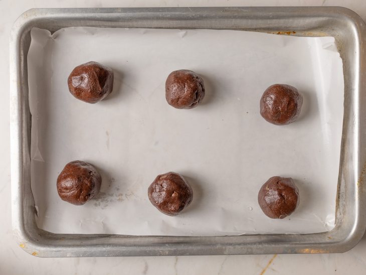 Porções de massa de cookie na forma forrada com papel-manteiga.