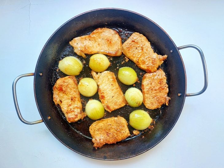 Uma frigideira fritando os filés e as cebolas.