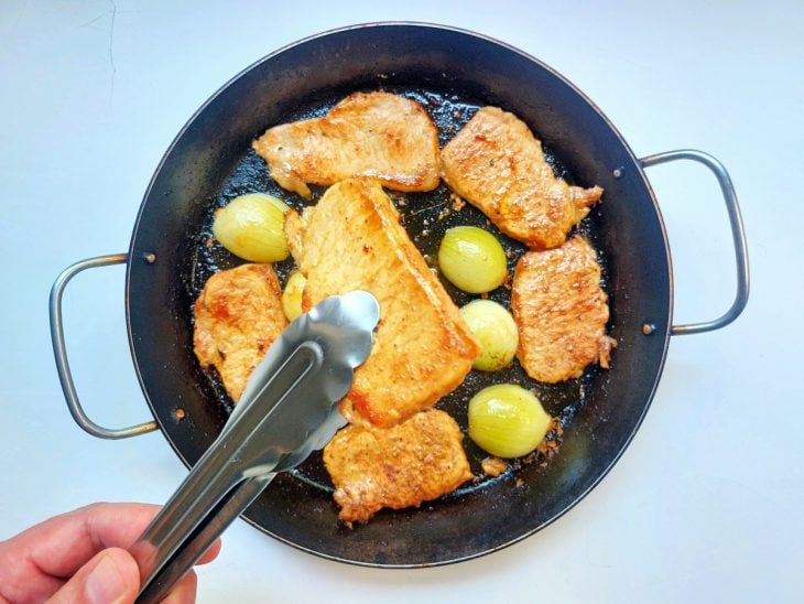 Uma frigideira fritando os filés e as cebolas.