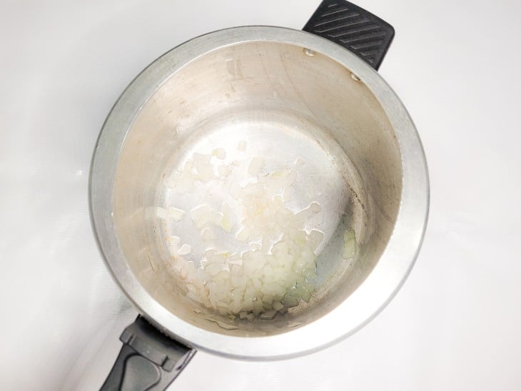 Uma panela de pressão com cebola picada sendo refogada no azeite.