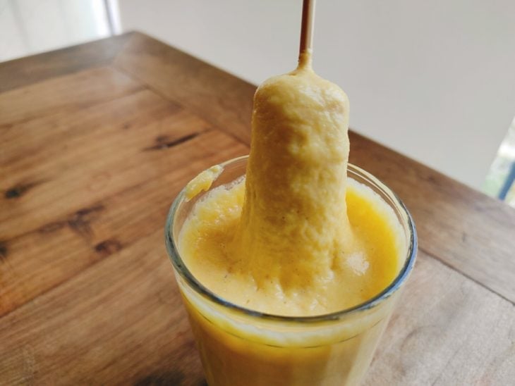 Palito com a salsicha sendo mergulhado no copo com a massa.