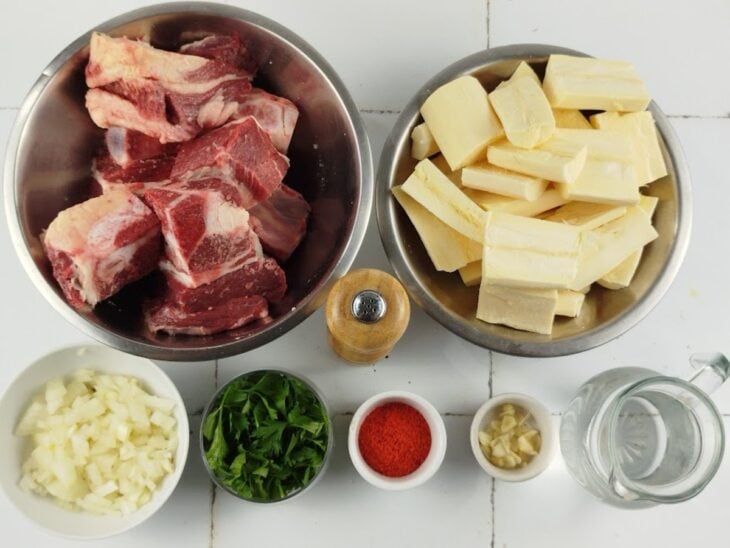 Bancada organizada com pedaços de costela, mandioca picada, cebola em cubos e alho na mesa.