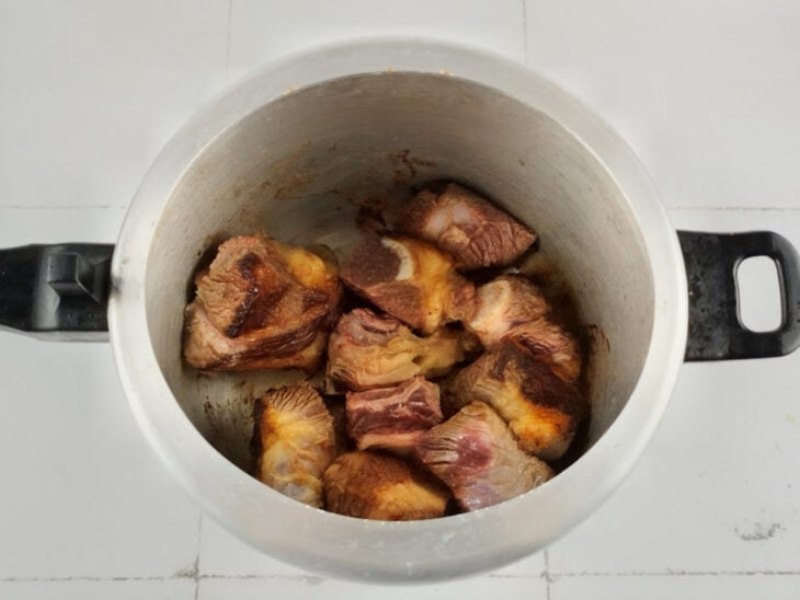 Pedaços de costela sendo fritos e dourados no óleo quente dentro da panela de pressão.
