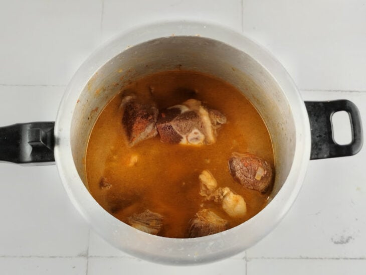 Água sendo despejada na panela sobre a carne para iniciar o cozimento sob pressão.