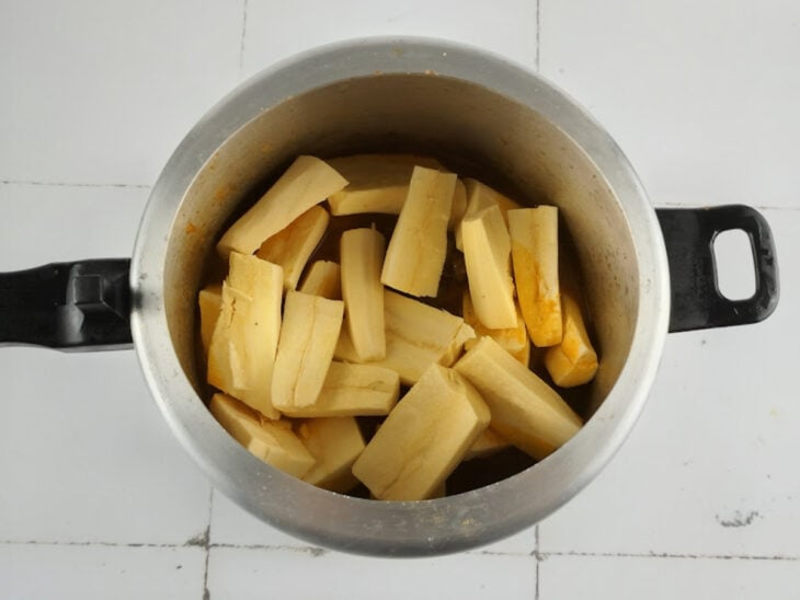 Panela de pressão aberta mostrando a costela cozida recebendo os pedaços de mandioca.