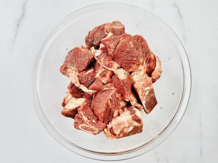 Pedaços de costela temperados em uma tigela de vidro redonda.