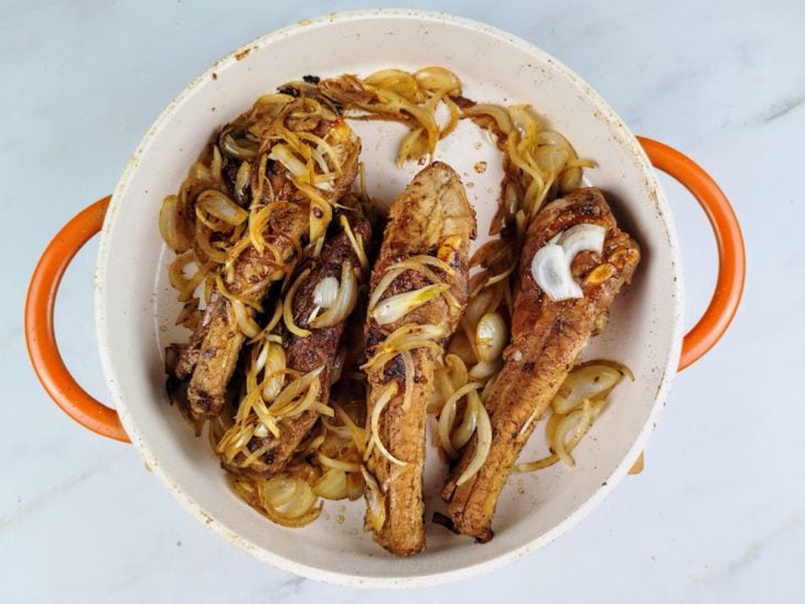 Panela com costelinhas e cebola fatiada.