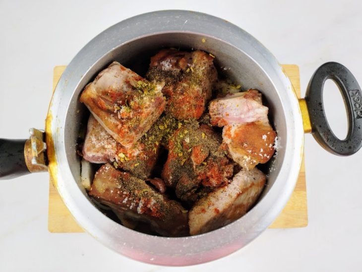 Costelinhas com temperos na panela com alho e cebola.