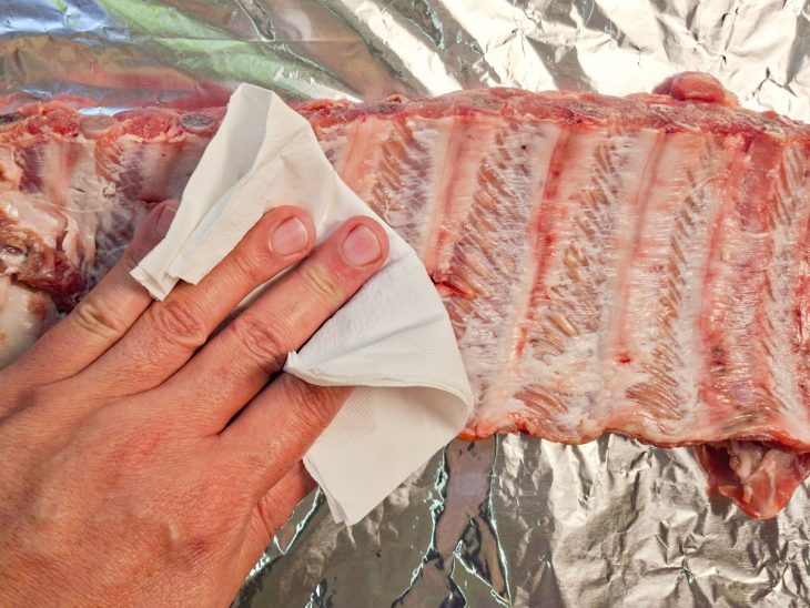 Costelinha sendo seca com papel-toalha antes de receber os temperos.