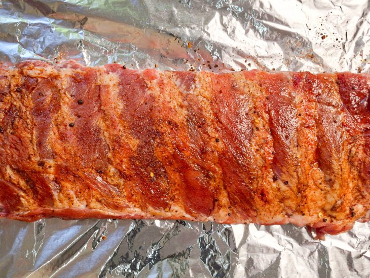 Dry rub sendo espalhado e pressionado sobre toda a superfície da carne.