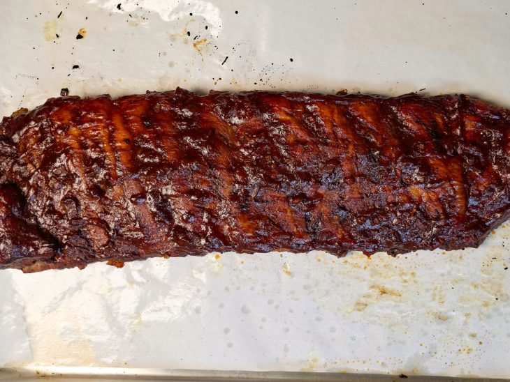 Molho barbecue sendo pincelado sobre a costelinha já dourada.