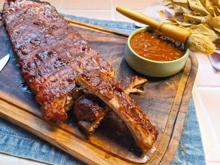 Costelinha servida com mais molho e acompanhamentos sobre a tábua.