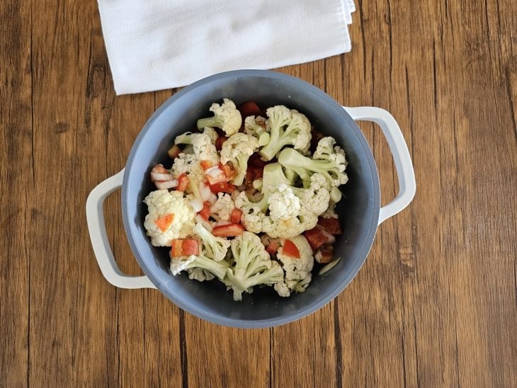 Uma panela contendo os buquês de couve-flor, óleo, sal, alho, cebola e tomates.