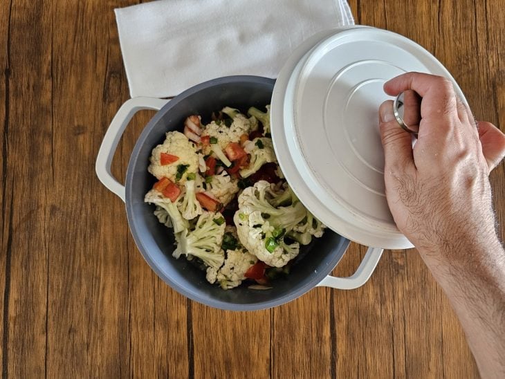 Uma panela contendo os buquês de couve-flor, óleo, sal, alho, cebola e tomates.