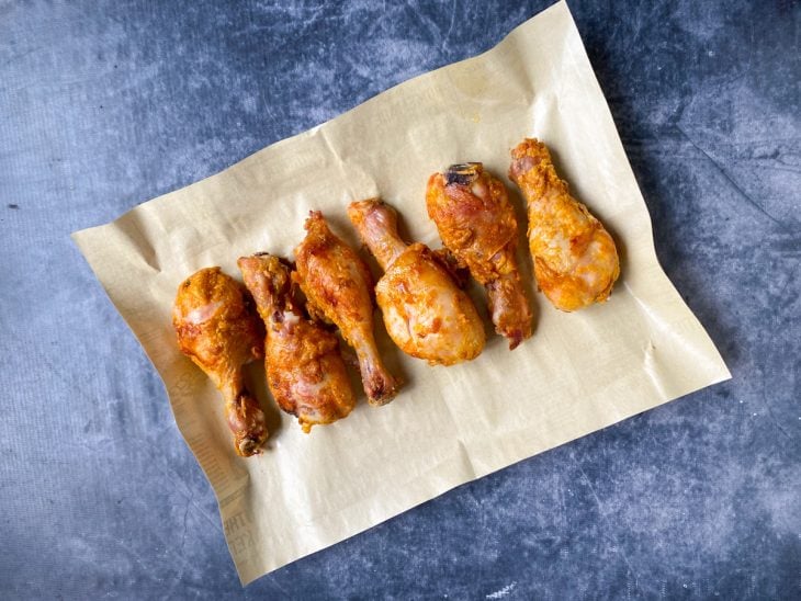 Uma assadeira forrada com papel contendo coxas de frango.