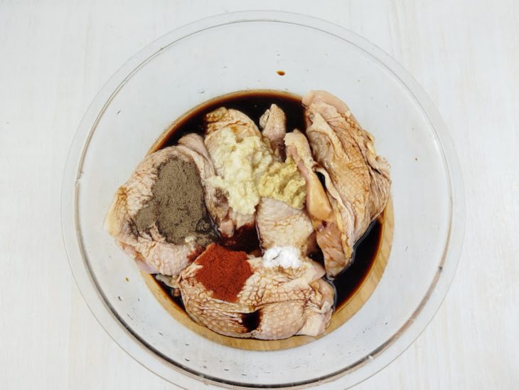 Frango na tigela sendo temperado com os ingredientes da marinada.