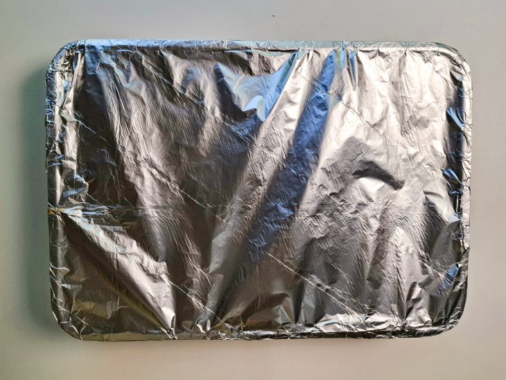 Assadeira com o frango coberta com papel alumínio.