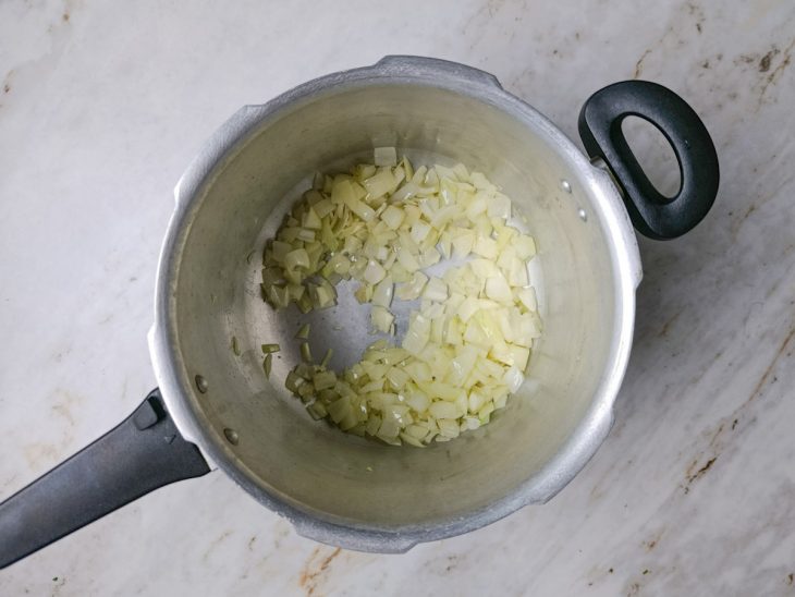 Cebola e alho refogando na panela de pressão com azeite.