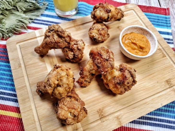 Coxinhas da asa prontas para consumo ao lado de um pequeno pote com molho de pimenta.