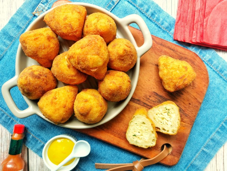 Várias coxinhas de batata-doce e uma aberta mostrando recheio.