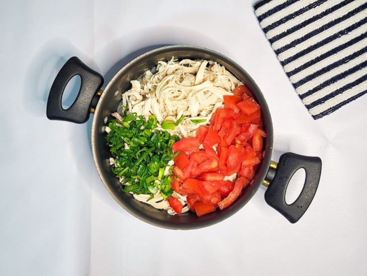 Uma panela com frango desfiado, tomate, ervas e sal.