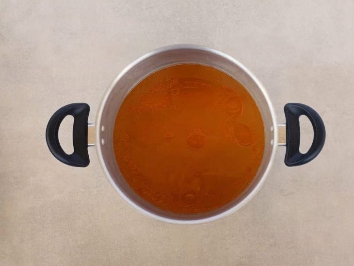 Caldo de frango aquecendo com óleo e colorau na panela.