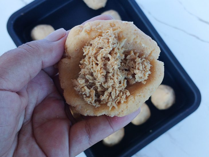 Massa sendo aberta na mão e recheada com frango desfiado.