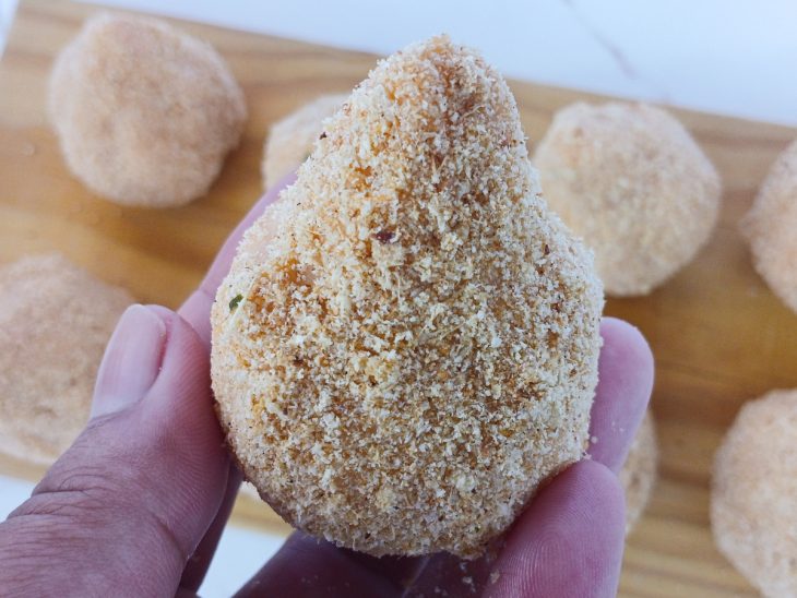 Coxinhas sendo passadas na clara de ovo e empanadas.