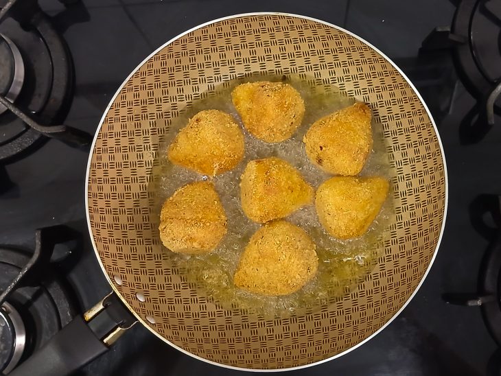 Coxinhas sendo fritas em óleo quente até dourar.