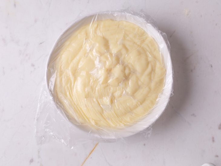 Um recipiente com o creme coberto com plástico filme.