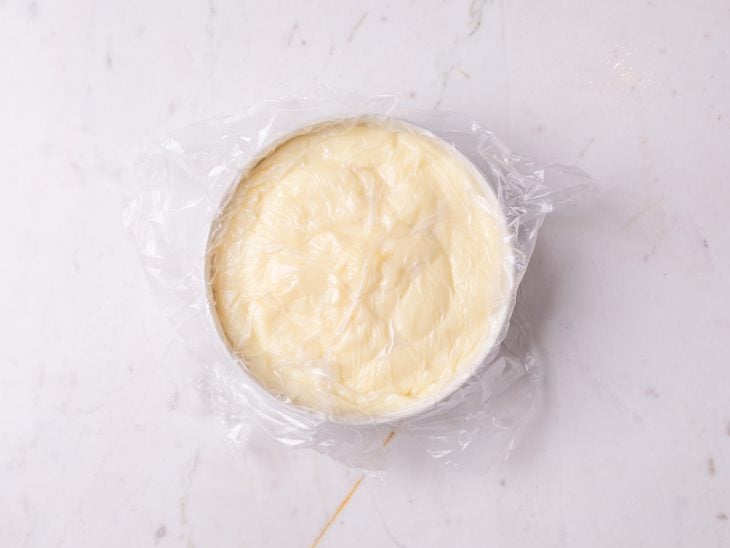 Um recipiente com o creme coberto com plástico filme.