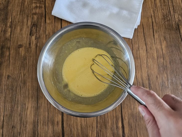 Gemas e açúcar misturados em uma tigela com um fouet.