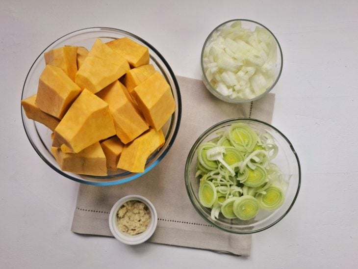 Abóbora, alho-poró, cebola e gengibre cortados em recipientes.