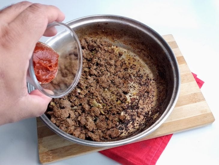 Uma frigideira com carne moída temperada e a adição de extrato de tomate.