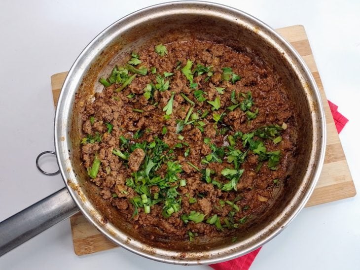 Uma frigideira com a carne moída pronta e cebolinha.