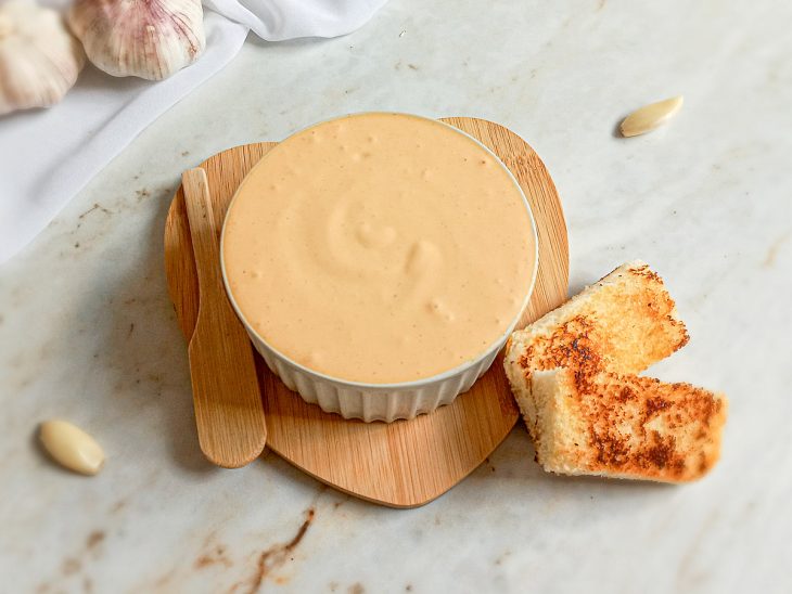 Creme de alho para pão pronto para consumo com fatias de pão tostadas ao lado.