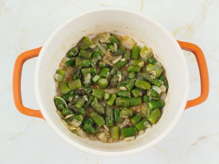 Alho e aspargos sendo refogados na panela.