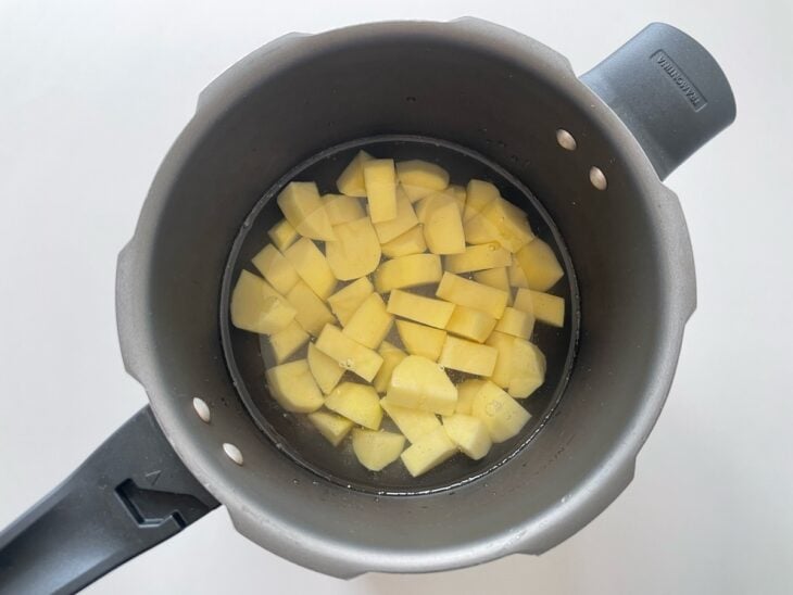 Batatas em cubos sendo colocadas dentro de uma panela de pressão e cobertas com água e sal.