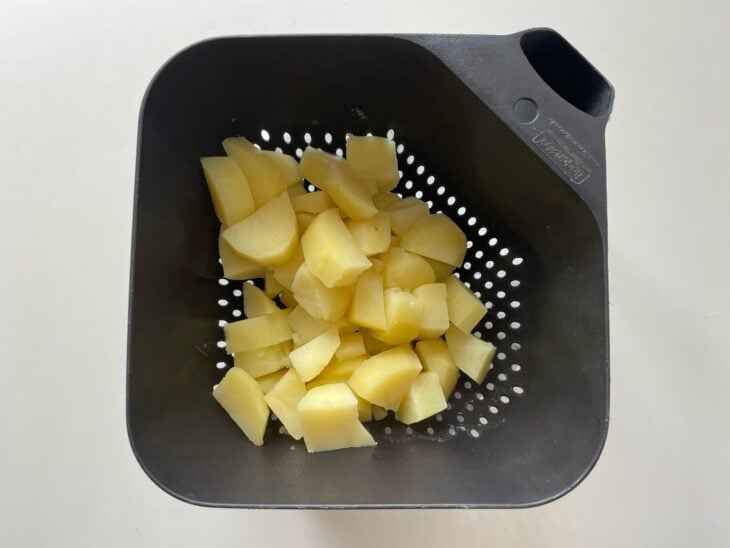Panela de pressão fechada sobre o fogão e, em seguida, as batatas cozidas e escorridas fumegando em um escorredor.