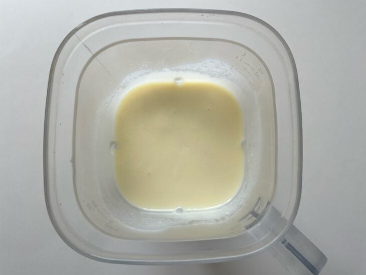 Leite morno, maionese, requeijão e as batatas cozidas sendo despejados juntos dentro do copo do liquidificador.