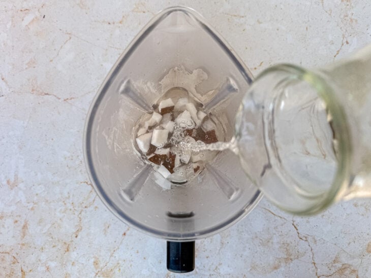 Pedaços de coco sendo colocados no liquidificador junto da água quente.