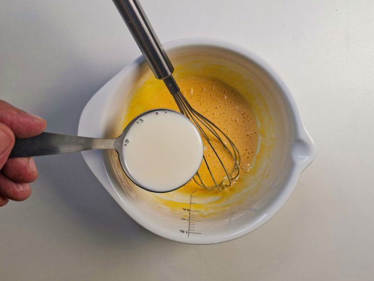Leite morno sendo adicionado aos poucos à mistura de ovos.