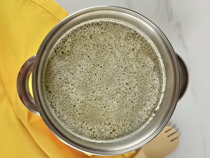 Uma panela com água, ervilhas, cebola, alho e louro.