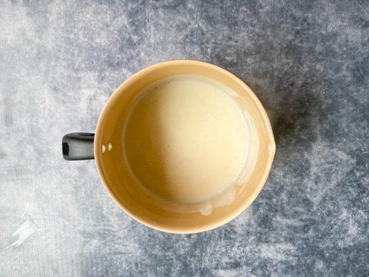 Uma caneca contendo a mistura de leite, Maizena, açúcar e baunilha.