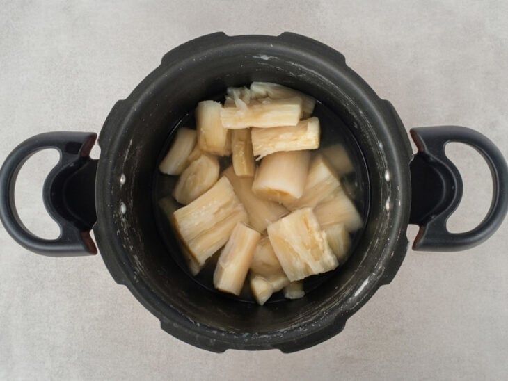 Mandioca cozinhando na panela de pressão até ficar muito macia e quase desmanchando.